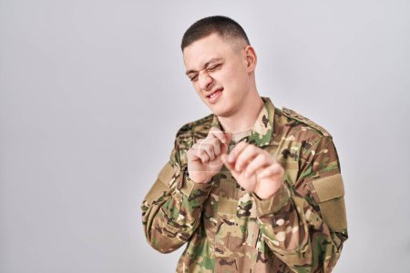 Téléchargez les photos : Jeune homme portant uniforme de camouflage de l'armée expression dégoûtée, mécontent et craintif faire face dégoût parce que réaction d'aversion. les mains levées - en image libre de droit