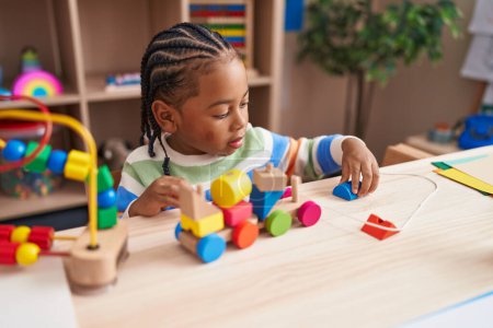 Foto de Chico afroamericano jugando con bloques tren juguete sentado en la mesa en el jardín de infantes - Imagen libre de derechos