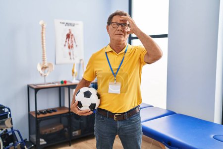 Photo for Senior man working at sport physiotherapy clinic stressed and frustrated with hand on head, surprised and angry face - Royalty Free Image