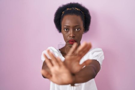 Téléchargez les photos : Femme africaine avec les cheveux bouclés debout sur fond rose expression de rejet croisant les bras et les paumes faisant signe négatif, visage en colère - en image libre de droit
