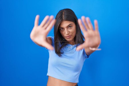 Téléchargez les photos : Brunette jeune femme debout sur fond bleu faisant cadre en utilisant les mains paumes et les doigts, perspective de la caméra - en image libre de droit