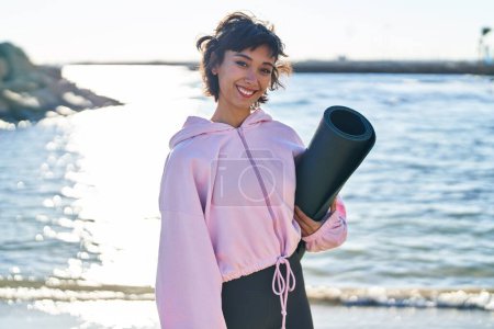 Foto de Mujer joven sosteniendo esterilla de yoga de pie junto al mar - Imagen libre de derechos