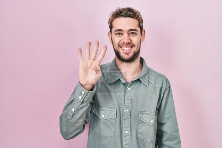 Téléchargez les photos : Homme hispanique avec barbe debout sur fond rose montrant et pointant vers le haut avec les doigts numéro quatre tout en souriant confiant et heureux. - en image libre de droit