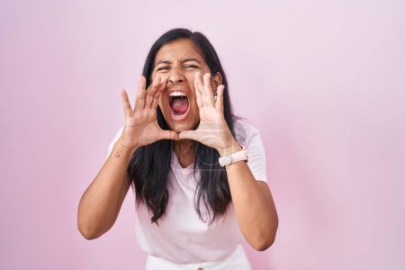 Foto de Mujer hispana joven de pie sobre fondo rosa gritando enojado en voz alta con las manos sobre la boca - Imagen libre de derechos