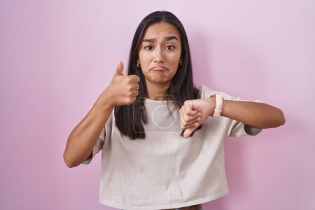 Photo for Young hispanic woman standing over pink background doing thumbs up and down, disagreement and agreement expression. crazy conflict - Royalty Free Image