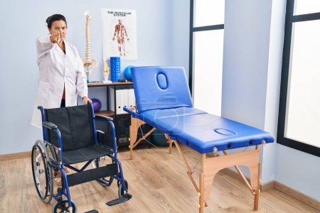 Photo for Middle age hispanic woman with wheelchair at physiotherapy clinic pointing with finger to the camera and to you, confident gesture looking serious - Royalty Free Image