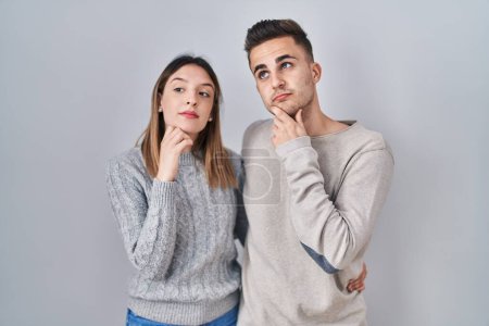 Photo for Young hispanic couple standing over white background with hand on chin thinking about question, pensive expression. smiling with thoughtful face. doubt concept. - Royalty Free Image