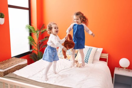 Foto de Adorables chicas sonriendo confiadas de pie en la cama en el dormitorio - Imagen libre de derechos