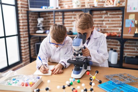 Téléchargez les photos : Adorables garçons étudiants utilisant des notes de microscope écriture à la salle de classe de laboratoire - en image libre de droit
