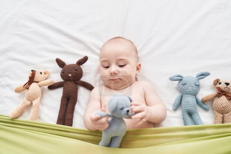 Téléchargez les photos : Adorable caucasian baby lying on bed with dolls at bedroom - en image libre de droit