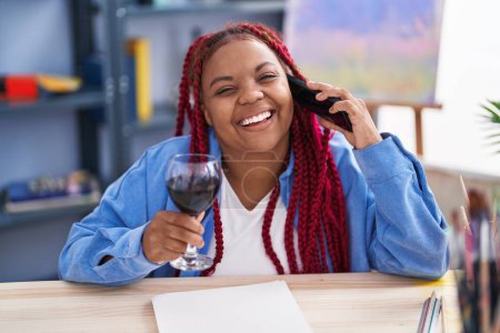 Téléchargez les photos : African american woman artist talking on smartphone drinking wine at art studio - en image libre de droit
