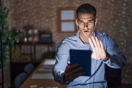 Téléchargez les photos : Bel homme hispanique travaillant au bureau la nuit faisant un geste d'arrêt avec les mains paumes de main, expression de colère et de frustration - en image libre de droit