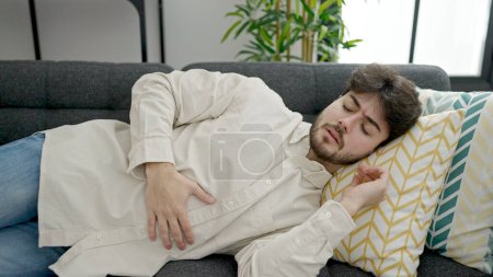 Photo for Young hispanic man suffering for stomach ache lying on sofa at home - Royalty Free Image