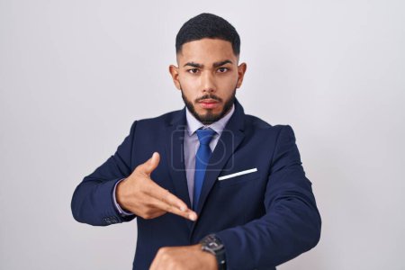 Téléchargez les photos : Jeune homme hispanique portant costume d'affaires et cravate à la hâte pointant pour regarder le temps, l'impatience, bouleversé et en colère pour retard de délai - en image libre de droit