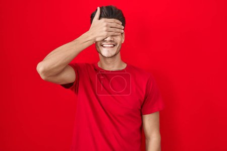 Photo for Young hispanic man standing over red background smiling and laughing with hand on face covering eyes for surprise. blind concept. - Royalty Free Image