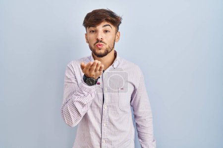 Foto de Arab man with beard standing over blue background looking at the camera blowing a kiss with hand on air being lovely and sexy. love expression. - Imagen libre de derechos