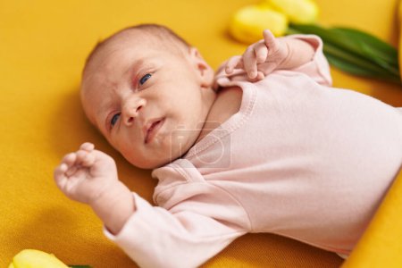 Téléchargez les photos : Adorable bébé hispanique couché sur le lit avec des fleurs dans la chambre - en image libre de droit