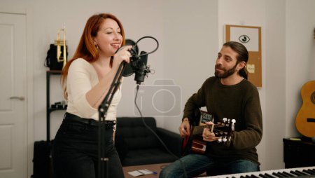 Foto de Man and woman singing son playing guitar at music studio - Imagen libre de derechos