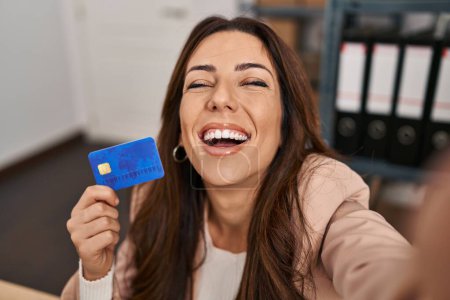 Photo for Young brunette woman working at small business ecommerce holding credit card smiling and laughing hard out loud because funny crazy joke. - Royalty Free Image