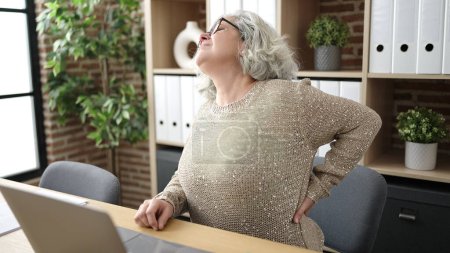 Foto de Mujer de mediana edad con trabajador de negocios de cabello gris que sufre de dolor de espalda en la oficina - Imagen libre de derechos