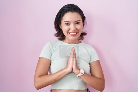 Photo for Hispanic young woman standing over pink background praying with hands together asking for forgiveness smiling confident. - Royalty Free Image