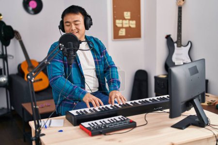 Téléchargez les photos : Young chinese man singer singing song playing piano keyboard at music studio - en image libre de droit