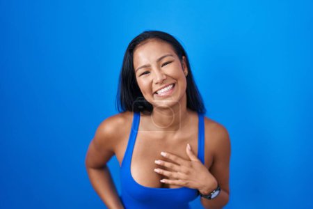 Téléchargez les photos : Femme hispanique debout sur fond bleu souriant et riant fort à haute voix parce que drôle blague folle avec les mains sur le corps. - en image libre de droit