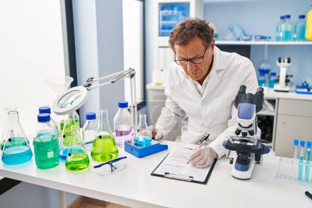 Photo for Middle age man wearing scientist uniform measuring test tube writing on clipboard at laboratory - Royalty Free Image