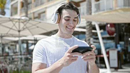 Foto de Joven hombre hispano sonriendo confiado viendo video en smartphone en la terraza de la cafetería - Imagen libre de derechos