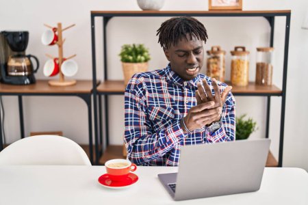 Téléchargez les photos : Afro-Américain souligné en utilisant un ordinateur portable assis sur la table à la maison - en image libre de droit