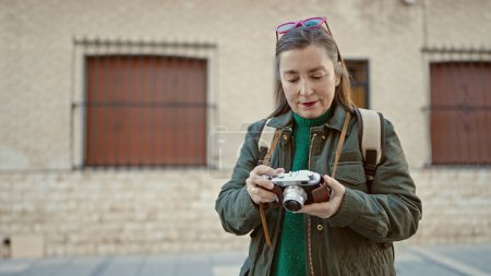 Foto de Mujer hispana madura con turista de pelo gris con mochila sosteniendo cámara vintage en la calle - Imagen libre de derechos