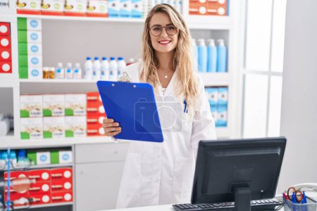 Téléchargez les photos : Jeune femme pharmacienne tenant presse-papiers travaillant à la pharmacie - en image libre de droit