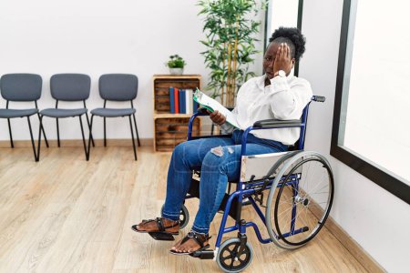 Photo for Young black woman sitting on wheelchair at waiting room yawning tired covering half face, eye and mouth with hand. face hurts in pain. - Royalty Free Image