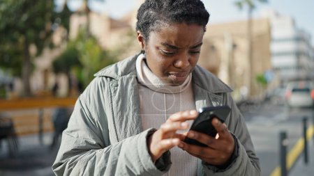 Téléchargez les photos : Femme afro-américaine utilisant un smartphone avec une expression sérieuse au parc - en image libre de droit