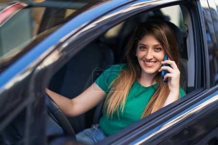 Téléchargez les photos : Jeune femme hispanique parlant sur le smartphone assis sur la voiture à la rue - en image libre de droit