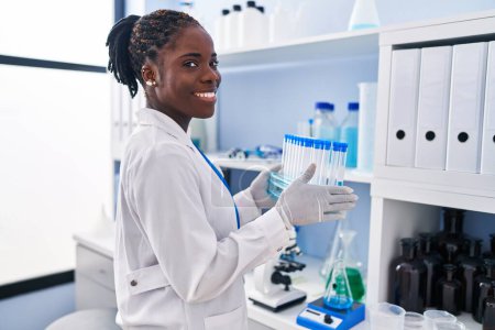 Téléchargez les photos : African american woman wearing scientist uniform holding test tubes at laboratory - en image libre de droit