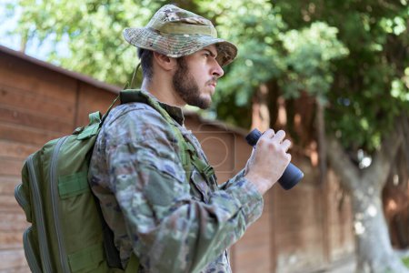 Photo for Young hispanic man wearing soldier uniform using binoculars at park - Royalty Free Image