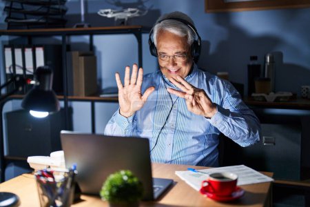 Photo for Hispanic senior man wearing call center agent headset at night showing and pointing up with fingers number eight while smiling confident and happy. - Royalty Free Image