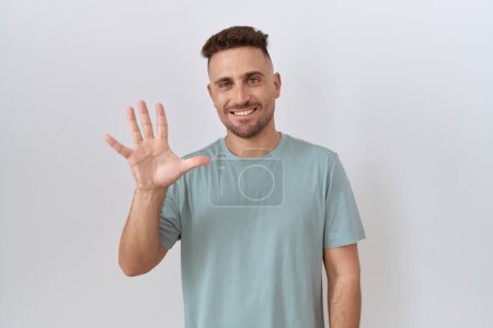 Foto de Hispanic man with beard standing over white background showing and pointing up with fingers number five while smiling confident and happy. - Imagen libre de derechos