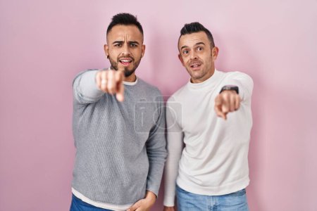 Photo for Homosexual couple standing over pink background pointing displeased and frustrated to the camera, angry and furious with you - Royalty Free Image