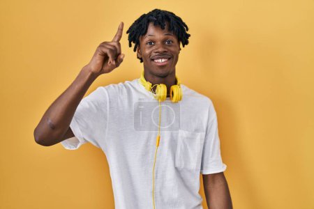 Téléchargez les photos : Jeune homme africain avec dreadlocks debout sur fond jaune pointant doigt vers le haut avec idée réussie. Sorti et heureux. numéro un. - en image libre de droit