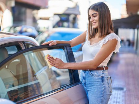 Photo for Young beautiful hispanic woman smiling confident cleaning glass window car at street - Royalty Free Image