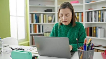 Téléchargez les photos : Femme hispanique mature aux cheveux gris utilisant un ordinateur portable à la bibliothèque - en image libre de droit