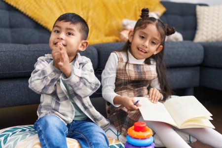 Téléchargez les photos : Adorable garçon et fille lecture livre applaudissements mains à la maison - en image libre de droit