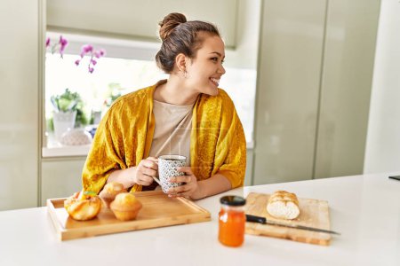 Photo for Young beautiful hispanic woman having breakfast drinking coffee at the kitchen - Royalty Free Image