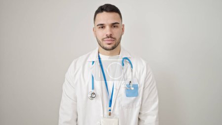 Foto de Joven médico hispano de pie con expresión seria sobre fondo blanco aislado - Imagen libre de derechos