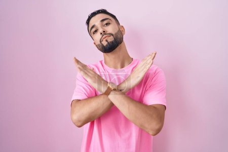 Photo for Hispanic young man standing over pink background rejection expression crossing arms doing negative sign, angry face - Royalty Free Image
