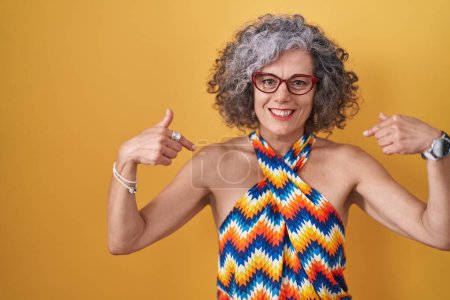 Photo for Middle age woman with grey hair standing over yellow background looking confident with smile on face, pointing oneself with fingers proud and happy. - Royalty Free Image