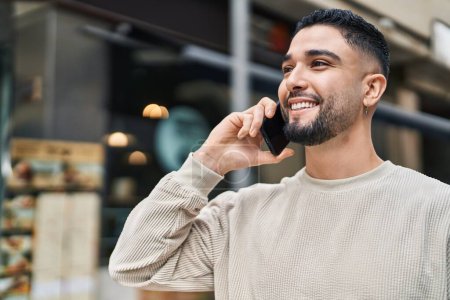 Photo for Young arab man smiling confident talking on the smartphone at street - Royalty Free Image