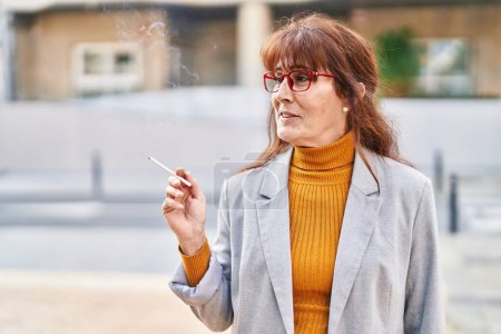 Photo for Middle age woman business executive smoking cigarette at street - Royalty Free Image
